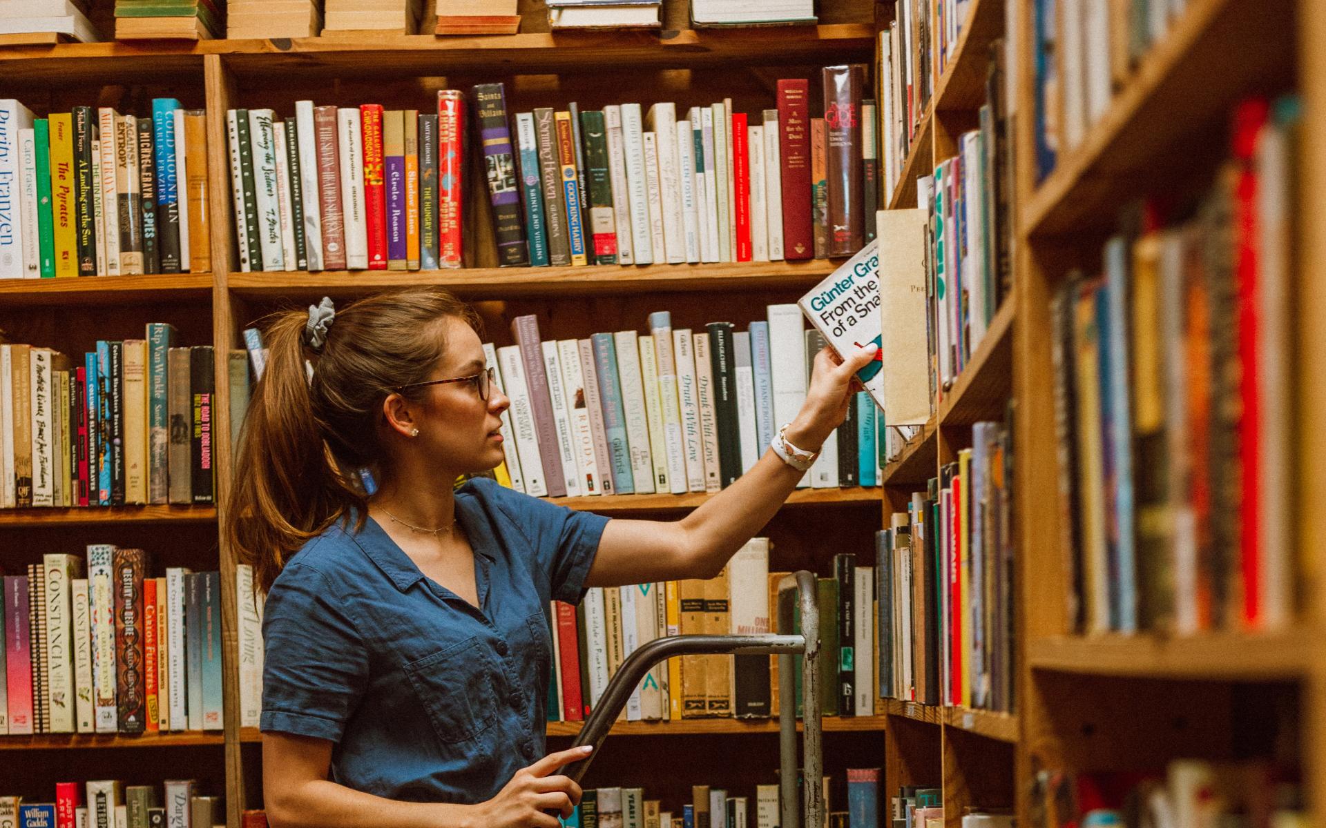 Junge Frau auf einer Leiter vor dem Bücherregal